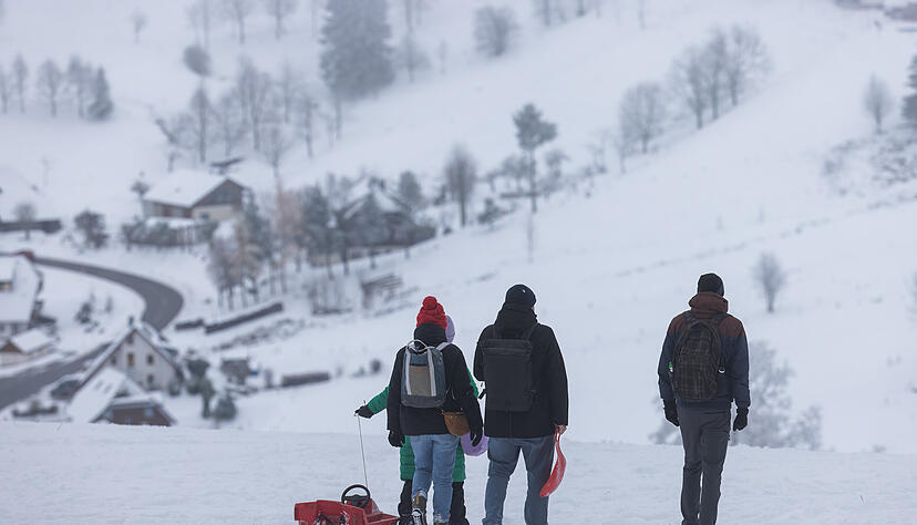 Menschen gehen mit einem Schlitten über eine verschneite Wiese auf dem Schauinsland. Schneefall lockt die Menschen derzeit nur in den Hochlagen vor die Haustüre. Doch das soll sich ändern.