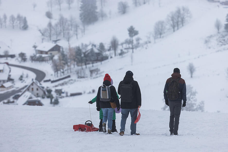 Menschen gehen mit einem Schlitten über eine verschneite Wiese auf dem Schauinsland. Schneefall lockt viele Menschen im Südwesten vor die Haustüre.