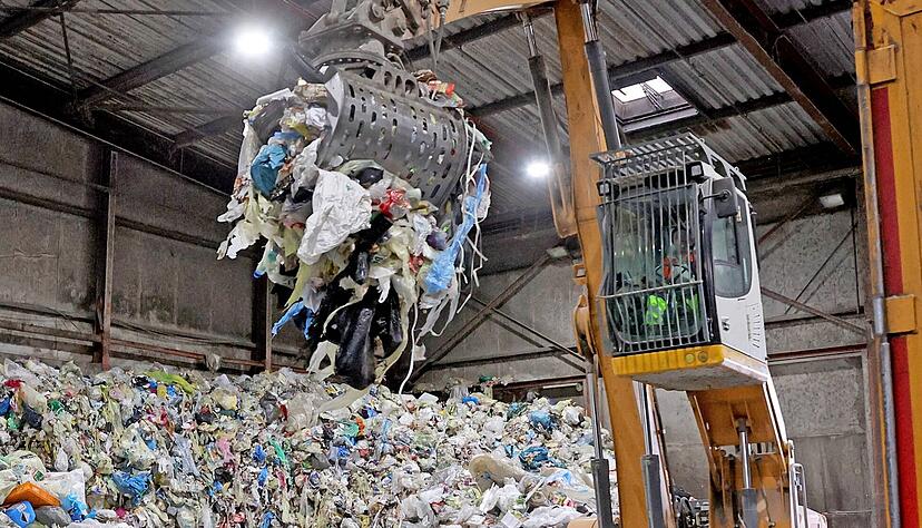 Mit einem Greifarm transportiert der Bagger die gelben Säcke in den Container eines Lastwagens, der den Abfall anschließend in eine Sortieranlage bringt.