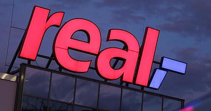Das Logo leuchtet am Morgen auf dem Dach eines Real Supermarktes.