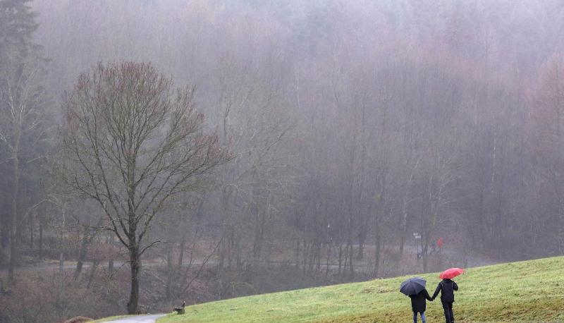 Spazierg&auml;nger sind mit Regenschirmen an einem nebligen tristen Wintertag unterwegs.