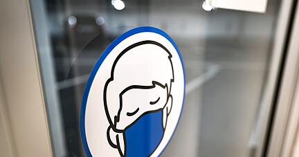 Ein Aufkleber an einer Glastür weist auf das Tragen einer Maske hin.