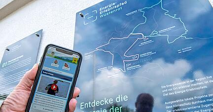 Die Station an der Burgfriedenhalle, an der eine Übersichtstafel und die Stationentafel angebracht sind. Mit den QR-Codes kommt man auf die App und die Infos zu Wärmepumpen, Lüftung und PV-Anlage.
Foto: Christiana Kunz