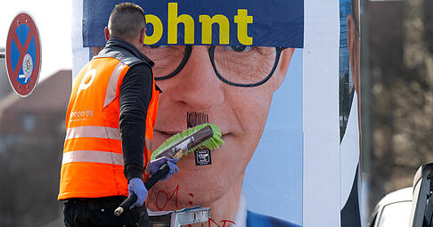Ein Mann überklebt nach der Bundestagswahl 2025 ein beschmiertes Wahlplakat der CDU mit dem Konterfei des Kanzlerkandidaten und CDU-Bundesvorsitzenden Merz.