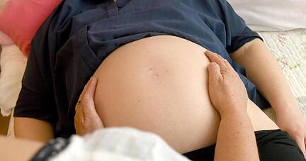 Eine Hebamme tastet den Bauch einer schwangeren Frau ab.