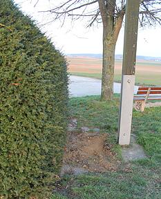 Brauner Fleck zwischen Hecke und Kreuz: Die Platte ist verschwunden. Brauner Fleck zwischen Hecke und Kreuz: Die Platte ist verschwunden.