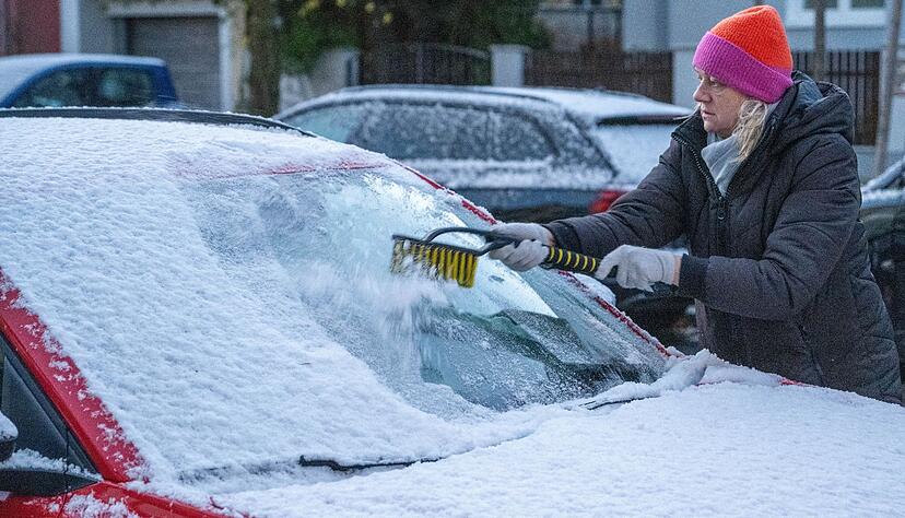 Eine Frau in München befreit am frühen Morgen ein Auto von Schnee und Eis. Auch in den kommenden Tagen soll es winterlich bleiben.