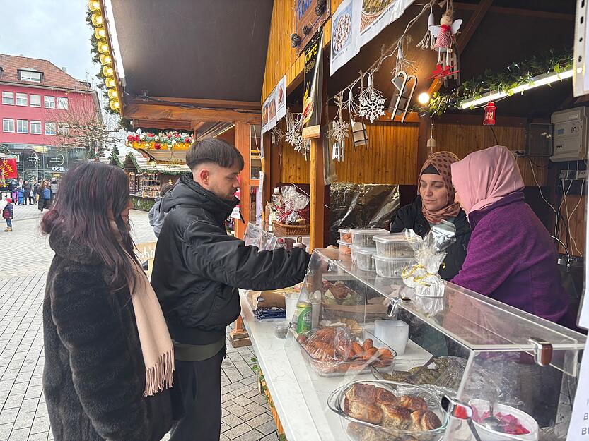 Kunden kaufen beim Stand des Horizont e.V. gefüllte Weinblätter und Köfte. In Cellophan eingewickelt stehen auf der Warenausgabe die selbstgemachten Dubai-Schokoladen.