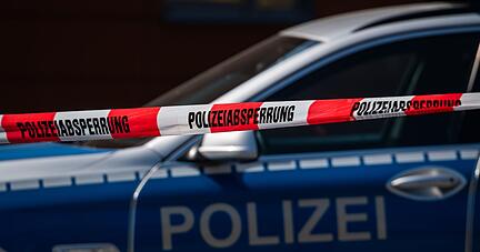 Ein Polizeiauto steht hinter einem Absperrband der Polizei.