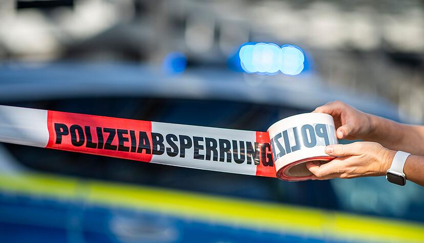 Ein Absperrband wird vor einem Polizeiwagen ausgerollt. Ein Absperrband wird vor einem Polizeiwagen ausgerollt.