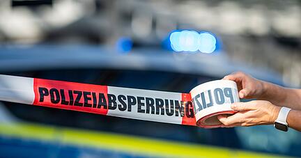Ein Absperrband wird vor einem Polizeiwagen ausgerollt.