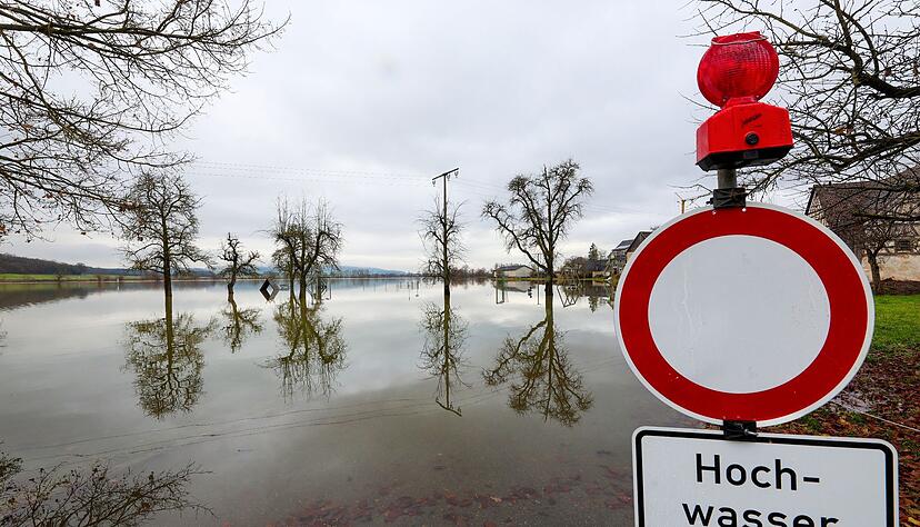 Hinter einem Durchfahrt verboten und Hochwasser-Hinweisschild, stehen Bäume im Wasser.