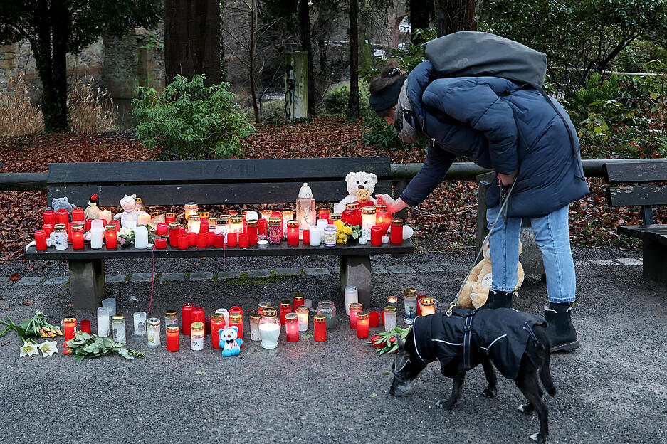 Eine Frau stellt eine Trauerkerze neben Blumen und Kuscheltieren nach dem tödlichen Angriff in einem Park am Tatort auf einer Bank ab.
