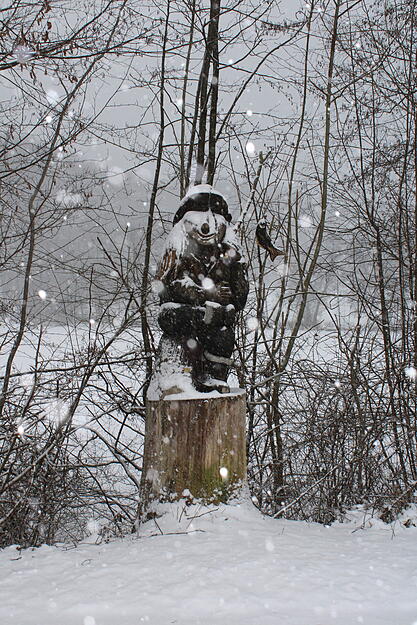 Am Neumühlsee ist der Angler aus Holz mit Schnee bedeckt.