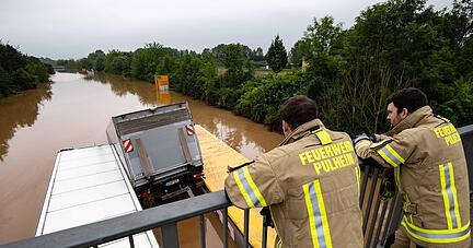 Feuerwehrleute blicken von einer Brücke auf die überflutete Bundesstraße 236.