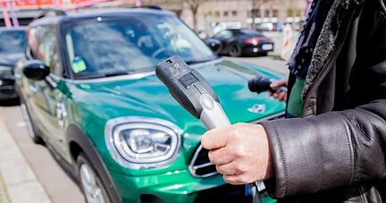 Ein Mann entfernt an einem Auto mit Plug-in-Hybrid-Antrieb in Berlin-Mitte das Ladekabel (Symbol).