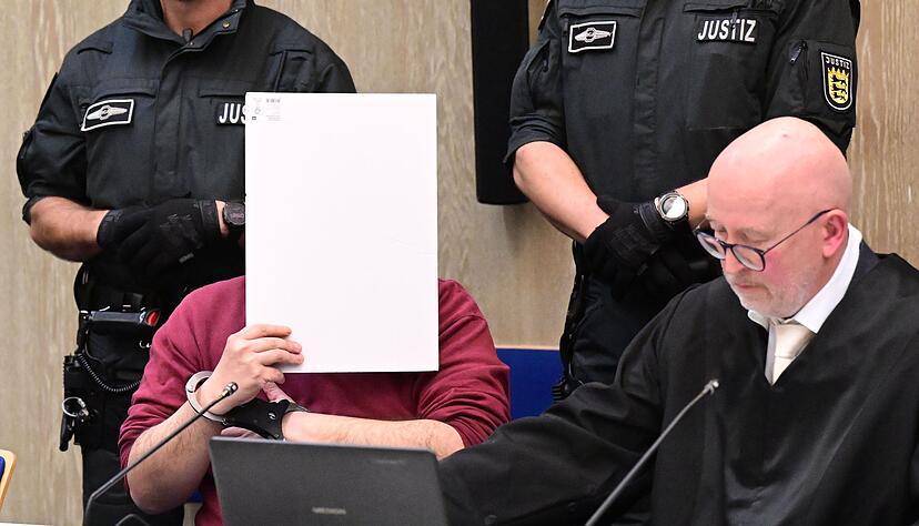Der Angeklagte in einem Mordprozess nach einer Todesfahrt von Mannheim sitzt mit einem Aktendeckel vor seinem Gesicht im Gerichtssaal, rechts neben ihm sitzt sein Verteidiger Uwe Kosmala. (Archivbild)