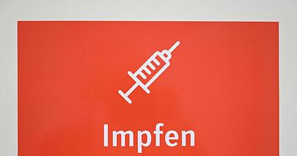 Ein Schild mit der Aufschrift "Impfen - Bitte warten! Sie werden aufgerufen." ist in einem Impfzentrum angebracht.