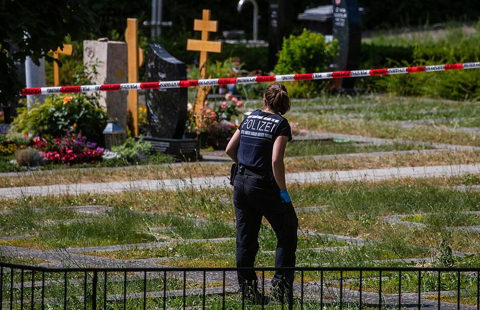 Eine Polizistin geht über den abgesperrten Teil an einem Tatort auf einem Friedhof. Durch den Wurf eines explodierenden Gegenstands auf eine Trauergemeinde gab es mehrere Verletzte. Eine Polizistin geht über den abgesperrten Teil an einem Tatort auf einem Friedhof. Durch den Wurf eines explodierenden Gegenstands auf eine Trauergemeinde gab es mehrere Verletzte.