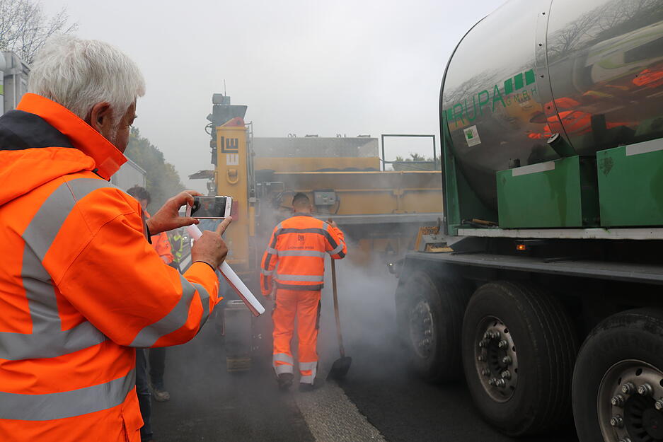 Regierungspr&auml;sident Wolfgang Reimer filmt. Er ist auf die Baustelle auf der A6 bei &Ouml;hringen gekommen, um zu sehen, wie erstmals bei einer Sanierung Gussasphalt eingebaut wird. &Uuml;blich ist Walzasphalt.