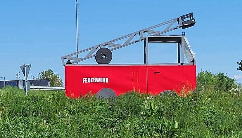 "Nehmt's mit Humor" steht auf einem Schild vor einer Attrappe eines Feuerwehrautos in einem Kreisverkehr in der Stadt Leingarten.