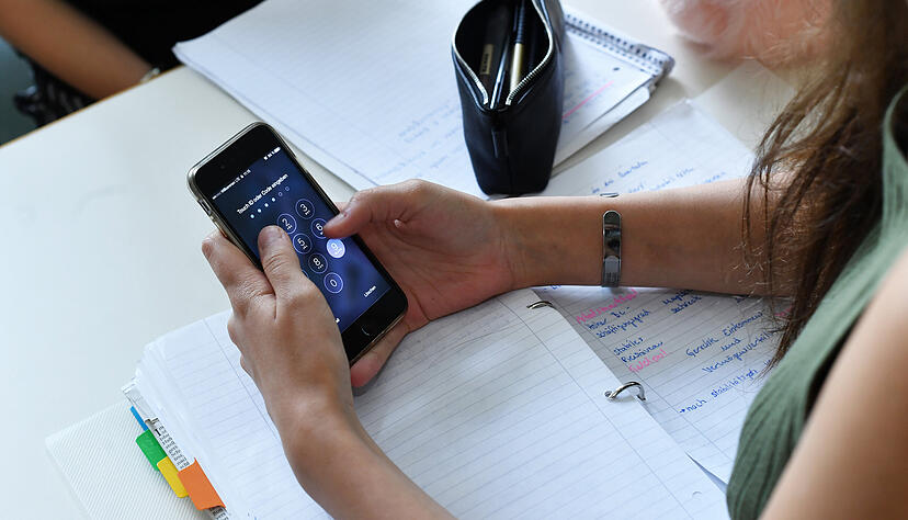 Eine Sch&uuml;lerin h&auml;lt im Unterricht ein Handy in den H&auml;nden. (Symbolbild)
