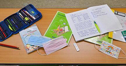 Unterrichtsmaterialien und Masken liegen während einer Pause auf einem Tisch in einer Grundschule.