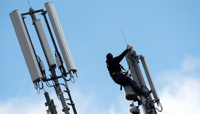 In luftiger H&ouml;he arbeiten zwei M&auml;nner an einem Mobilfunkmast, der auf dem Dach eines Geb&auml;udes steht.