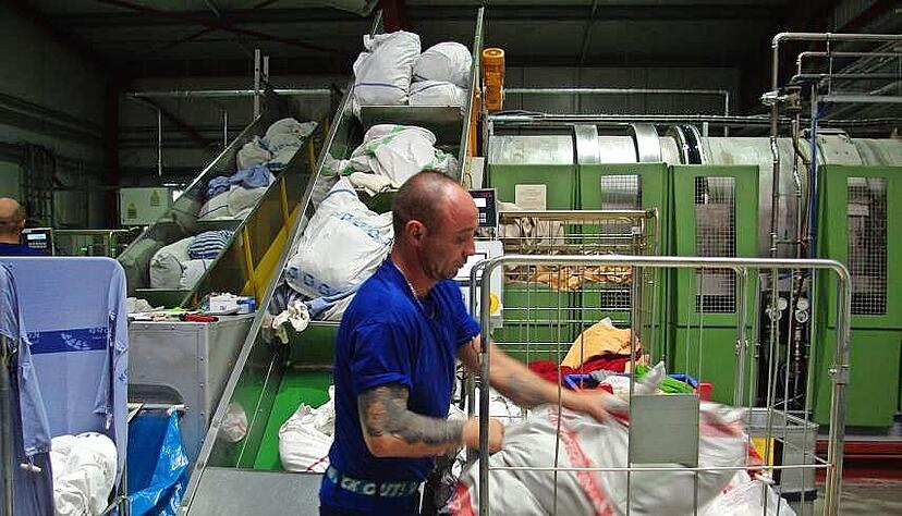 G&uuml;nter Ebers wuchtet routiniert S&auml;cke mit Bettw&auml;sche und Handt&uuml;chern auf das F&ouml;rderband zur Waschmaschine.