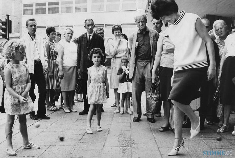Juni 1966: Neugierige Zuschauer versammeln sich vor dem Warenhaus. Der Ol&eacute;-Swing verursacht in den USA gro&szlig;en Wirbel. Man l&auml;sst einen an der Schnur befestigten kleinen Ball um den Kn&ouml;chel des einen Fu&szlig;es kreisen und springt mit dem anderen Bein dar&uuml;ber hinweg. Die Herstellerfirma pr&auml;sentiert das Spiel bei Merkur.