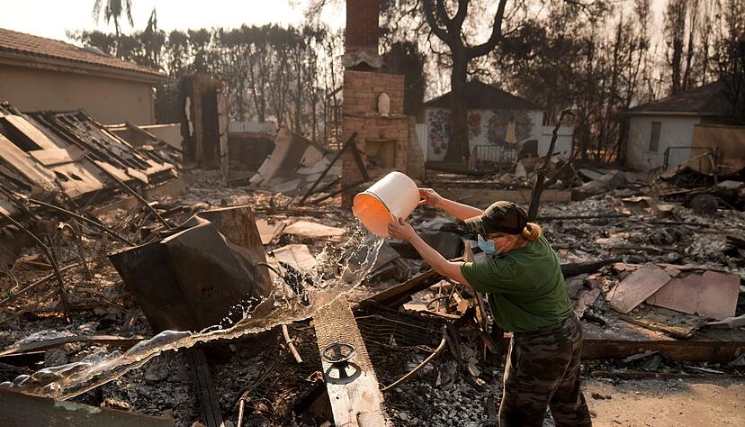 Nancy Belanger gie&szlig;t Wasser auf das vom Feuer verw&uuml;stete Grundst&uuml;ck eines Nachbarn im Stadtteil Pacific Palisades von Los Angeles.