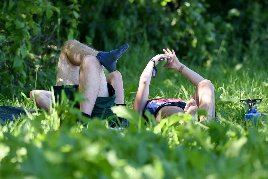 Zwei Festivalbesucher liegen im Gras unter Schatten spendenden B&auml;umen.