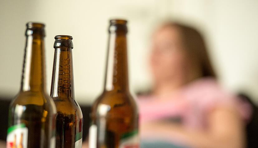 Eine junge Frau sitzt hinter leeren Bierflaschen. Die Corona-Krise förderte den Alkohol-Verkauf in vielen Ländern. Foto: dpa