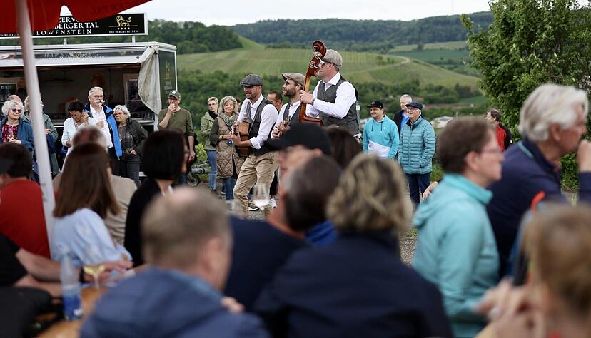 Querfeldwein 2024: Trauben von Menschen um die Musiker "The Bohemians". Mit Ukulele, Gitarre und Kontrabass kamen sie letztes Jahr mit ihren mitrei&szlig;enden Kl&auml;ngen am Erlenbacher Kayberg hervorragend an.