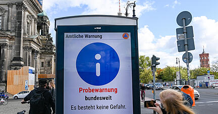 "Probewarnung bundesweit. Es besteht keine Gefahr" steht beim ersten bundesweiten Warntag auf einer Informationstafel Unter den Linden, die von einer Frau fotografiert wird. In ganz Deutschland findet der Probealarm mittels Informationstafeln, Sirenen, Warn-Apps, Radio, Fernsehen und über soziale Medien statt. Ziel ist es, Warntechnik für besondere Risiken zu testen. +++ dpa-Bildfunk +++