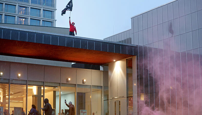 Ein Demonstrant hat es auf das Dach der Harmonie geschafft und schwenkt eine Fahne.