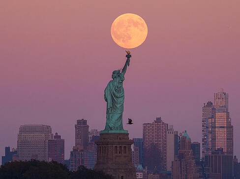 Der Supermond geht hinter der Freiheitsstatue in den USA über der Skyline von Brooklyn auf.