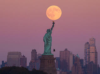Der Supermond geht hinter der Freiheitsstatue in den USA über der Skyline von Brooklyn auf.