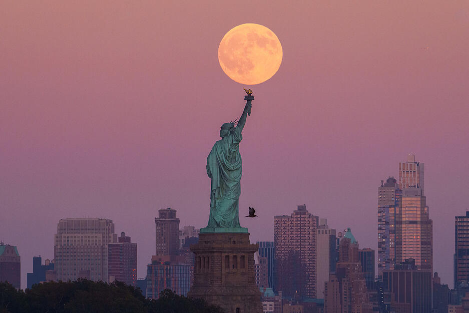 Der Supermond geht hinter der Freiheitsstatue in den USA über der Skyline von Brooklyn auf.
