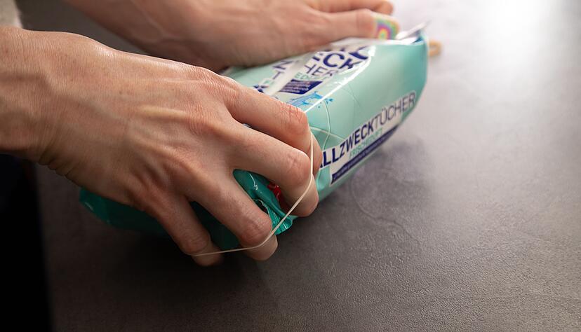 So geht's: Gummibänder links und rechts von der Öffnung der Verpackung anbringen. So geht's: Gummibänder links und rechts von der Öffnung der Verpackung anbringen.