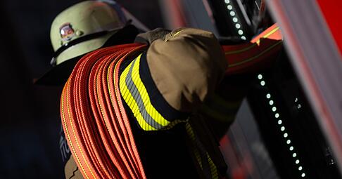 Eine Einsatzkraft der Feuerwehr nimmt einen Schlauch aus einem Einsatzfahrzeug.