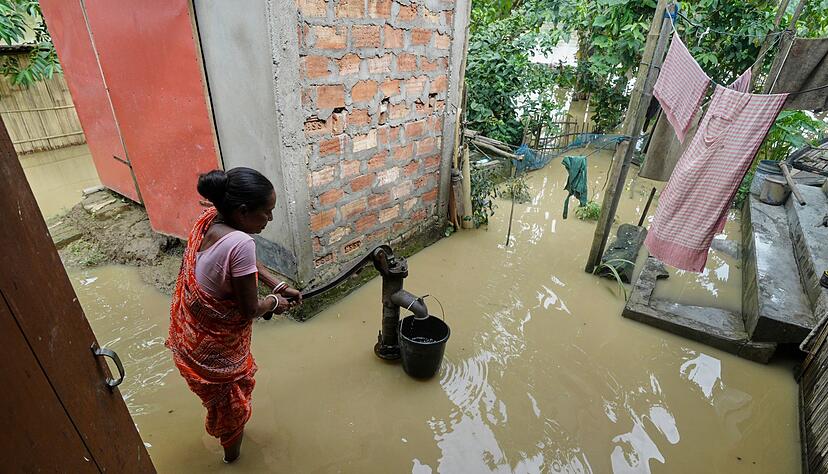Eine Frau versucht in der &uuml;berfluteten Umgebung ihres Hauses, Wasser zu sammeln.