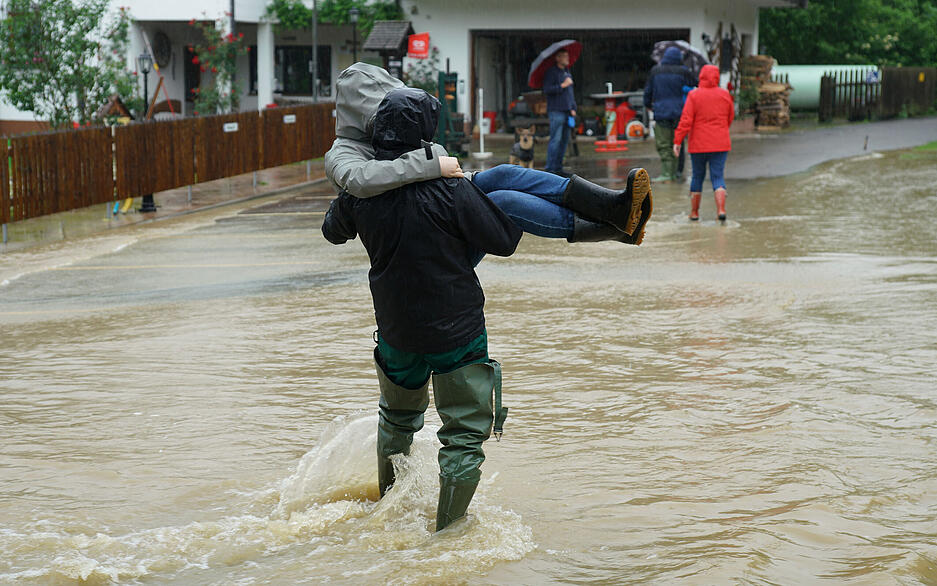 Ein Mensch trägt eine Person durch Hochwasser in Albershausen im Landkreis Göppingen. Hier wurde auch ein Minigolfplatz überschwemmt.