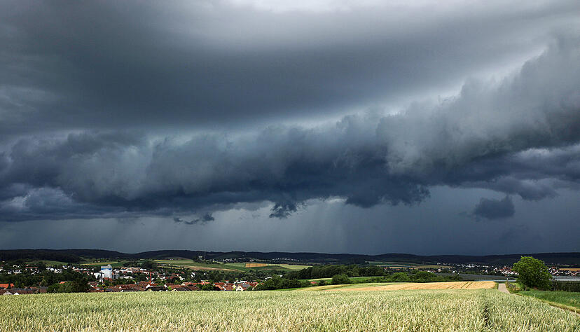 Eine Gewitterzelle mit dunklen Wolken baut sich am Himmel und hinter Feldern nahe Heilbronn auf.