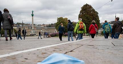 Ein Mundschutz liegt auf dem Stuttgarter Schlossplatz auf dem Boden, dahinter zahlreiche Passanten. Ein Mundschutz liegt auf dem Stuttgarter Schlossplatz auf dem Boden, dahinter zahlreiche Passanten.