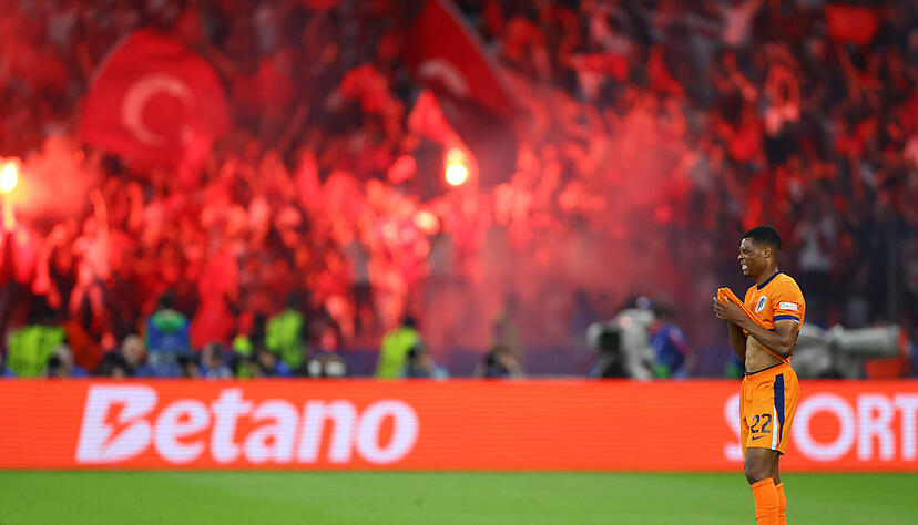 Die türkischen Fans zünden Pyrotechnik. Der niederländische Spieler steht für einen Moment auf dem Spielfeld still da.