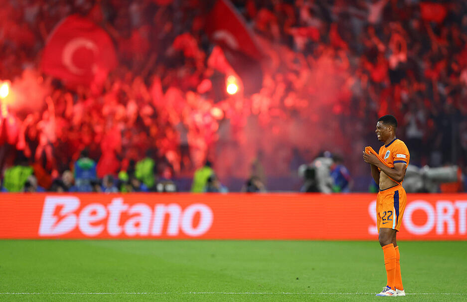 Die türkischen Fans zünden Pyrotechnik. Der niederländische Spieler steht für einen Moment auf dem Spielfeld still da.