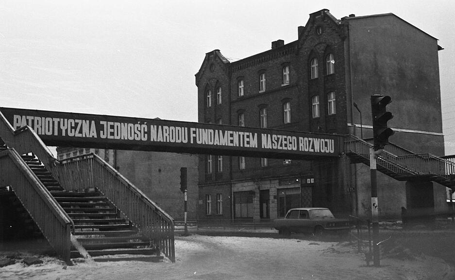 In Kattowitz, auf dem Weg in ein Waisenhaus, f&auml;hrt die Heilbronner Delegation an einem gigantischen Banner mit dem Spruch: "Die patriotische Einheit des Volkes ist das Fundament unserer Entwicklung." vorbei. Die Stadt ist Zentrum des gewaltigen Bergbau- und H&uuml;ttenreviers. Im Winter erscheint sie noch trostloser. Aufnahme von Dezember 1981.