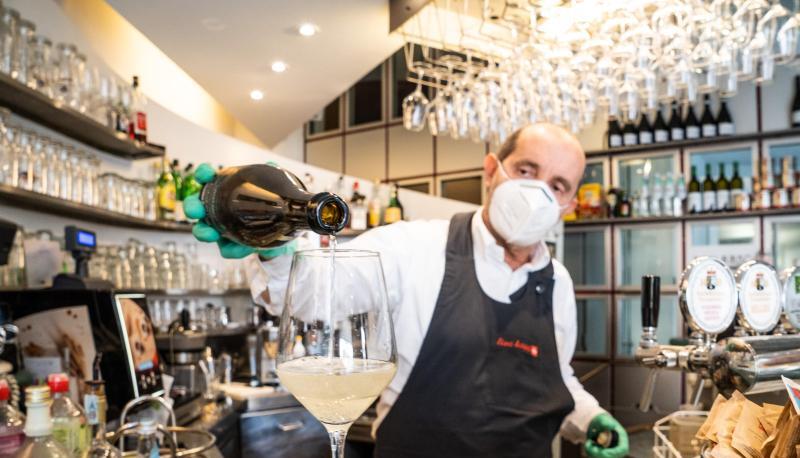 Ein Barmann mit Atemschutzmaske schenkt in Bozen ein Glas Wein ein. (Archivbild). Ein Barmann mit Atemschutzmaske schenkt in Bozen ein Glas Wein ein. (Archivbild).