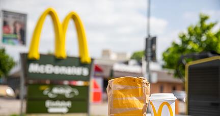 Eine McDonald's To-go-Tüte und ein dazugehöriger To-go-Becher stehen vor einer Tübinger McDonald's Filiale.